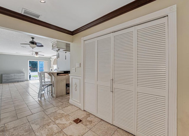 kitchen with ceiling fan, a kitchen bar, ornamental molding, a textured ceiling, and light tile patterned floors