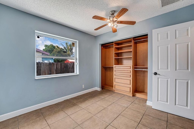 unfurnished bedroom with ceiling fan, a textured ceiling, light tile patterned floors, and a closet