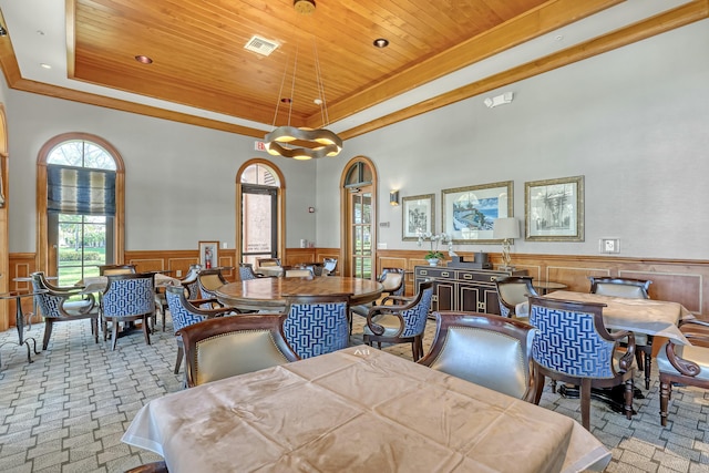 dining space with a tray ceiling, wooden walls, light colored carpet, and wooden ceiling