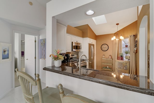 kitchen featuring white cabinetry, hanging light fixtures, kitchen peninsula, vaulted ceiling with skylight, and appliances with stainless steel finishes