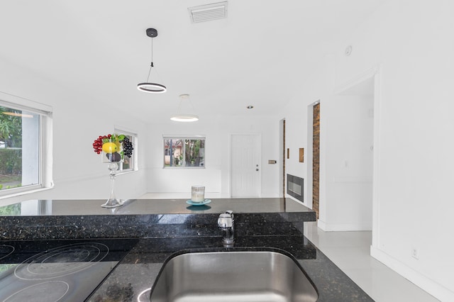 kitchen with sink, hanging light fixtures, light tile patterned floors, and dark stone countertops