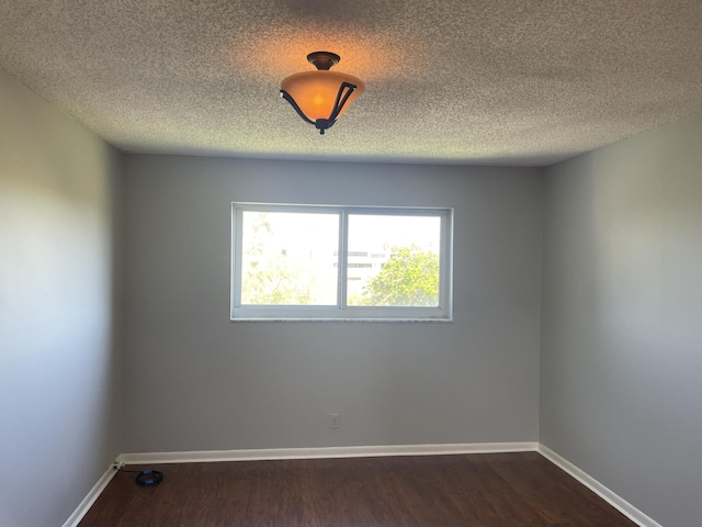 unfurnished room with a textured ceiling, dark wood-style flooring, and baseboards