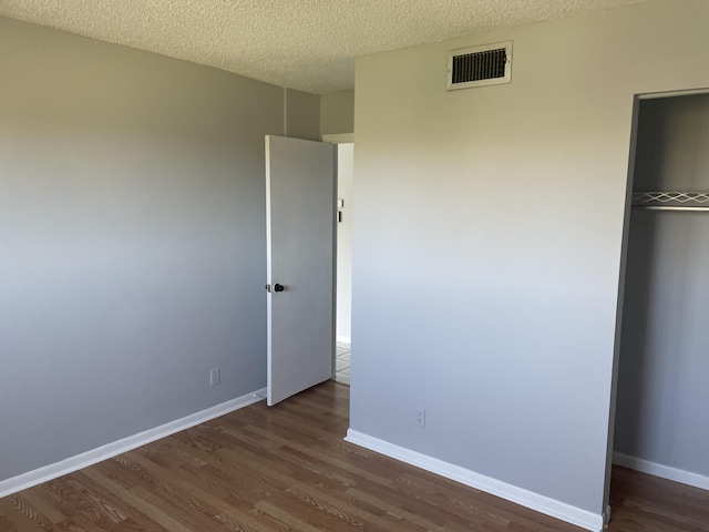 unfurnished bedroom with a textured ceiling, wood finished floors, visible vents, baseboards, and a closet