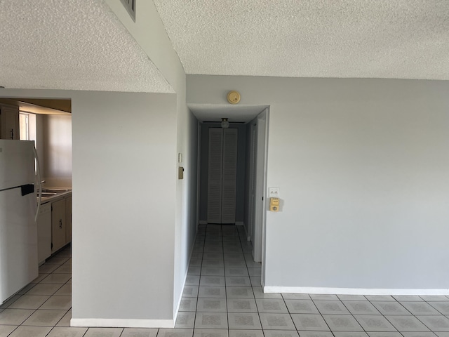 empty room featuring a textured ceiling, baseboards, and light tile patterned floors