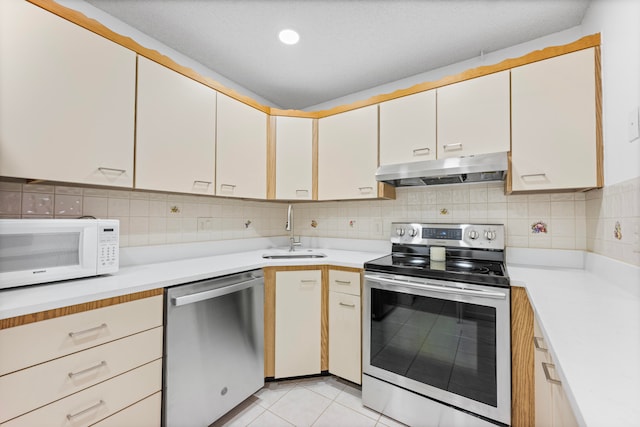 kitchen with appliances with stainless steel finishes, tasteful backsplash, sink, light tile patterned floors, and white cabinetry