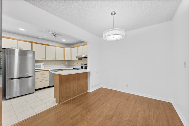 kitchen with hanging light fixtures, ceiling fan, light wood-type flooring, appliances with stainless steel finishes, and kitchen peninsula