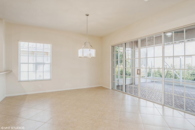 empty room with plenty of natural light, light tile patterned flooring, and a chandelier