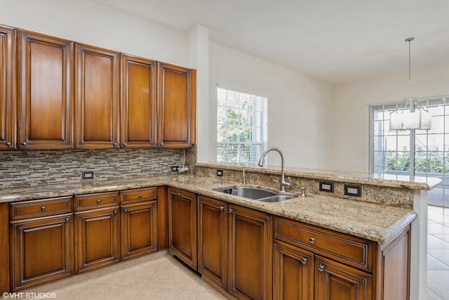 kitchen featuring pendant lighting, light stone counters, kitchen peninsula, and sink