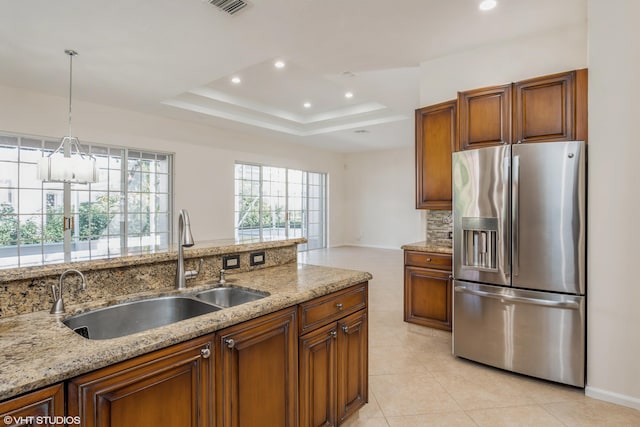 kitchen featuring sink, stainless steel refrigerator with ice dispenser, hanging light fixtures, light stone countertops, and a tray ceiling