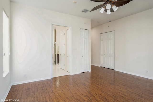 unfurnished bedroom with multiple closets, ceiling fan, and dark hardwood / wood-style floors