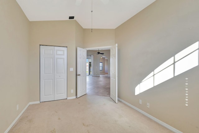 unfurnished bedroom featuring light carpet, a closet, ceiling fan, and a high ceiling