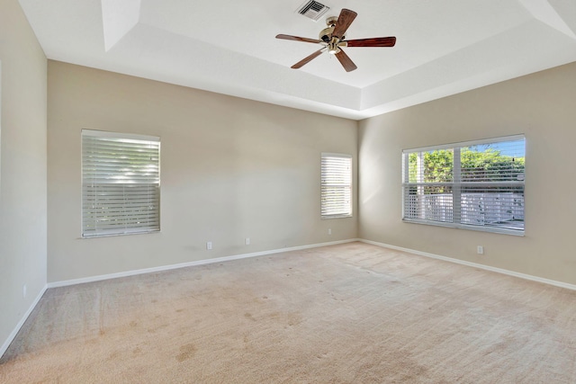 unfurnished room with ceiling fan, a raised ceiling, and light carpet