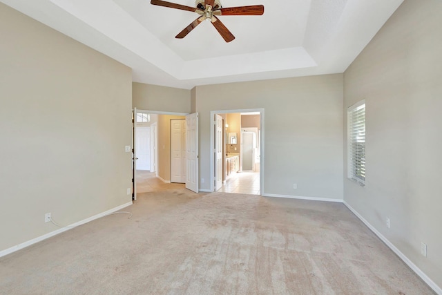 empty room with a raised ceiling, ceiling fan, and light carpet