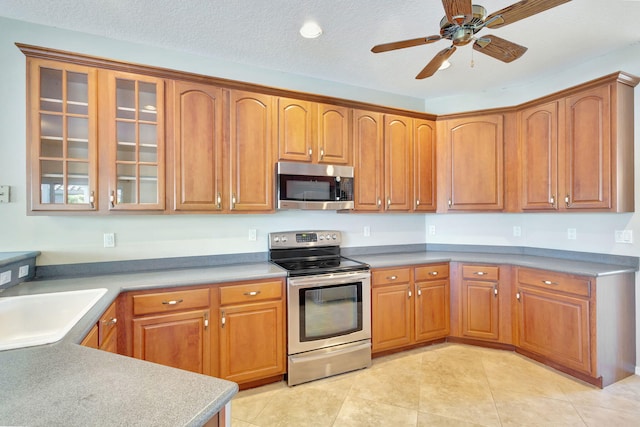 kitchen featuring ceiling fan, sink, a textured ceiling, light tile patterned floors, and appliances with stainless steel finishes