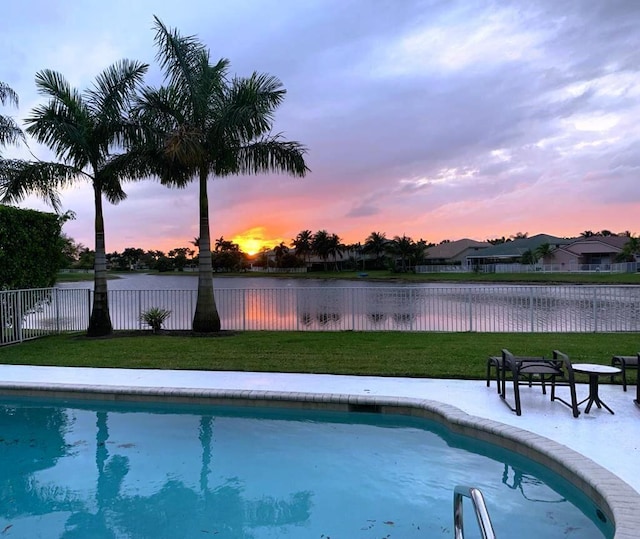 pool at dusk featuring a water view and a lawn