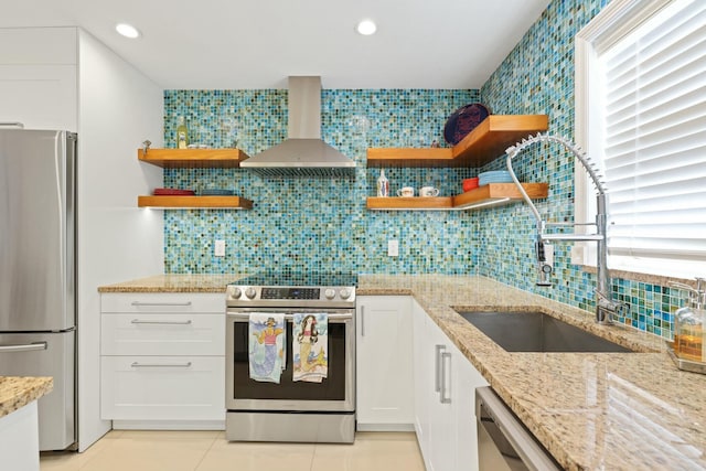 kitchen with white cabinets, wall chimney exhaust hood, light stone countertops, and stainless steel appliances