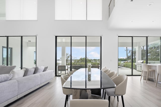 dining space with light wood-type flooring and a towering ceiling