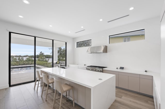 kitchen with a kitchen breakfast bar, wall chimney range hood, sink, gray cabinets, and light wood-type flooring