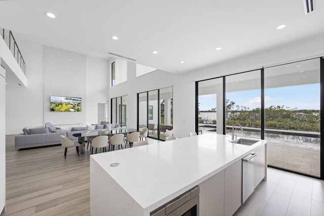 kitchen featuring stainless steel microwave, a kitchen island with sink, sink, light hardwood / wood-style flooring, and white cabinetry