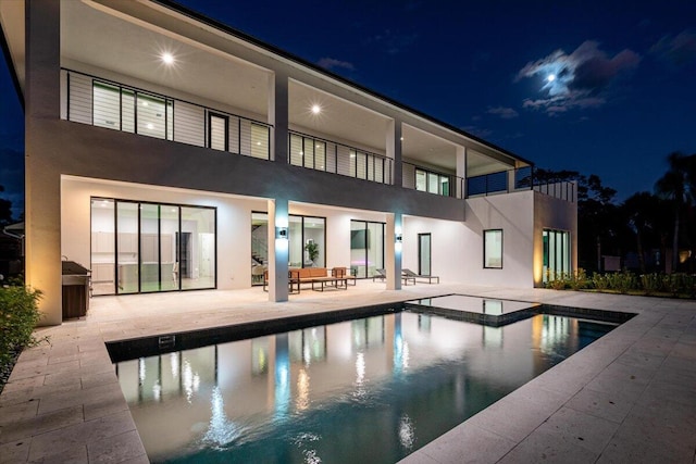 back house at twilight featuring a patio, an outdoor hangout area, and a pool with hot tub