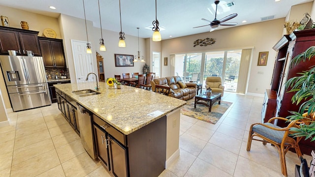 kitchen with a kitchen island with sink, sink, hanging light fixtures, light stone counters, and stainless steel appliances