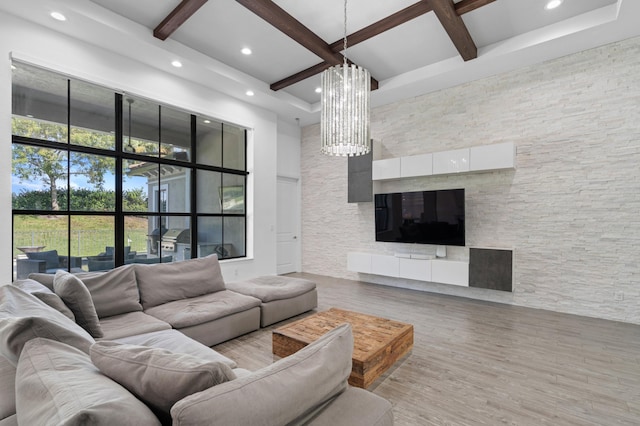 living room featuring hardwood / wood-style floors, a notable chandelier, beamed ceiling, a high ceiling, and a stone fireplace