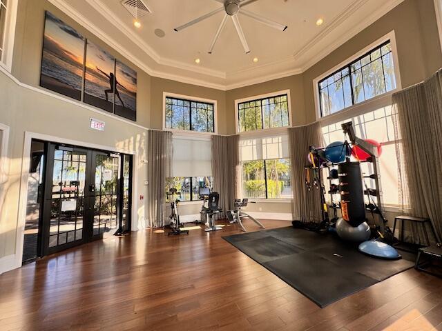 workout area featuring ceiling fan, wood-type flooring, ornamental molding, and a towering ceiling