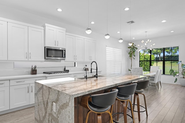 kitchen with hanging light fixtures, white cabinetry, stainless steel appliances, and a kitchen island with sink