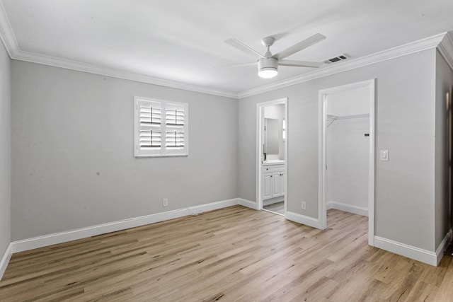 unfurnished bedroom with ceiling fan, a walk in closet, crown molding, and light hardwood / wood-style flooring