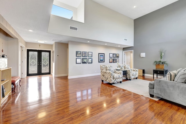 living room with french doors, a towering ceiling, and hardwood / wood-style flooring