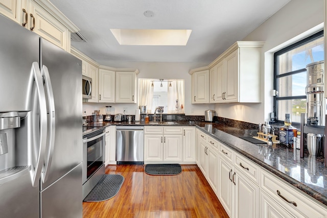 kitchen featuring dark stone counters, sink, a skylight, appliances with stainless steel finishes, and wood-type flooring