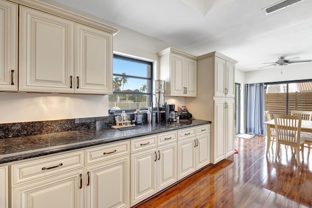 kitchen with ceiling fan, dark stone countertops, dark wood-type flooring, and cream cabinets