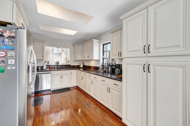 kitchen with dark wood-type flooring, dark stone counters, a skylight, appliances with stainless steel finishes, and white cabinetry