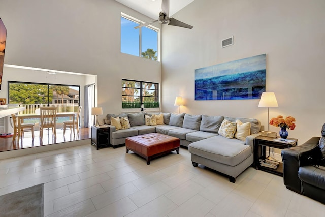 tiled living room with ceiling fan and a high ceiling