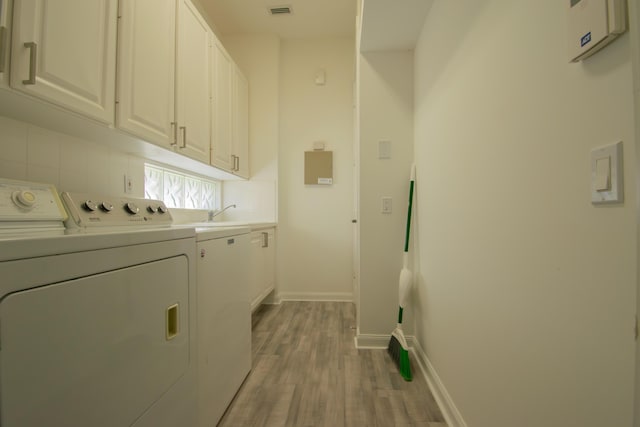 laundry room featuring washing machine and dryer, visible vents, baseboards, light wood-type flooring, and cabinet space