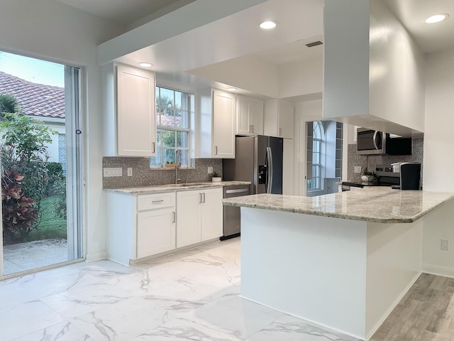 kitchen with appliances with stainless steel finishes, white cabinetry, a peninsula, and light stone counters