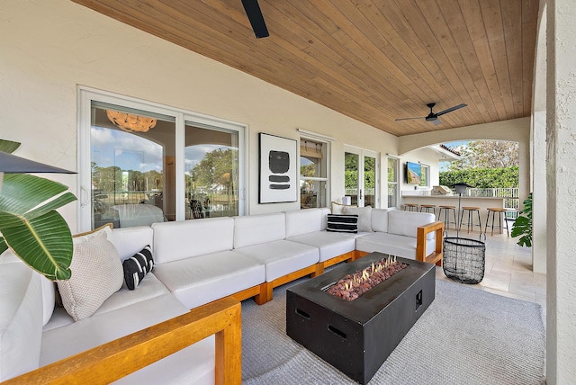 view of patio with ceiling fan, a bar, and an outdoor living space with a fire pit