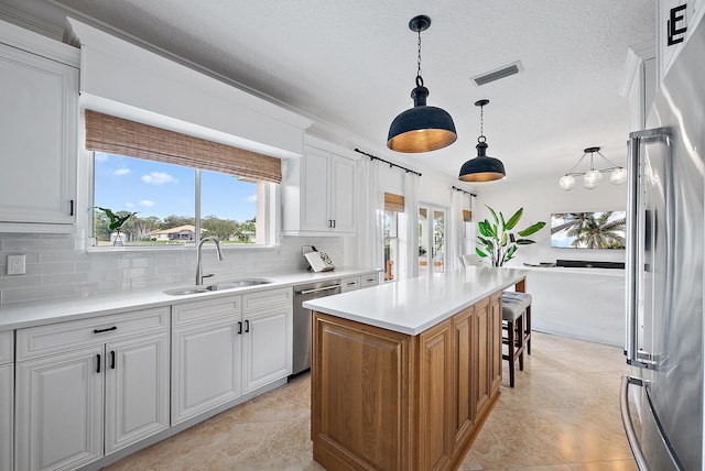 kitchen featuring appliances with stainless steel finishes, a kitchen island, sink, decorative light fixtures, and white cabinetry