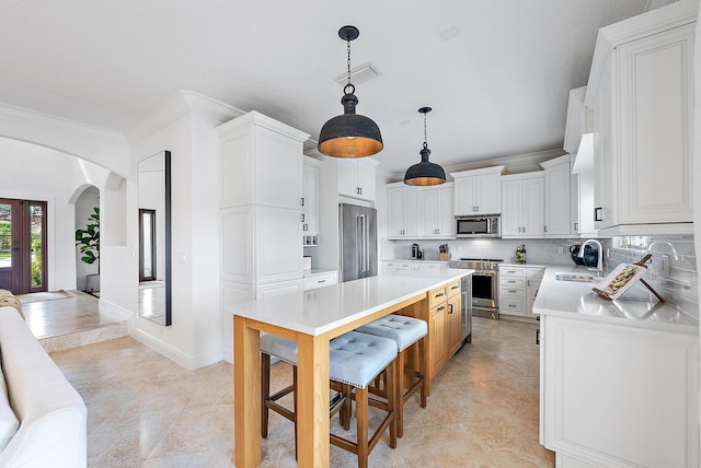 kitchen with a center island, sink, stainless steel appliances, decorative light fixtures, and white cabinets