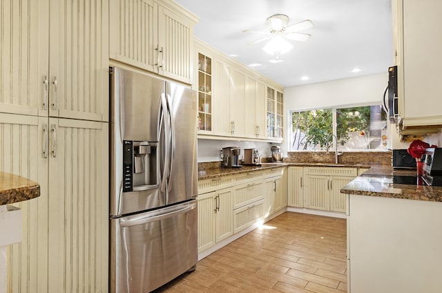 kitchen featuring dark stone counters, stainless steel fridge with ice dispenser, cream cabinets, light wood-style floors, and a sink