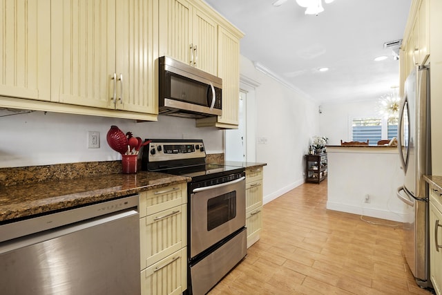 kitchen with baseboards, light wood-style flooring, appliances with stainless steel finishes, ornamental molding, and cream cabinets