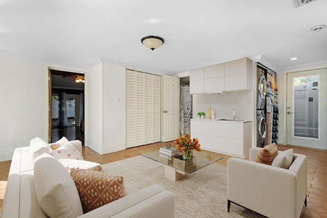 living room featuring crown molding, stacked washer and clothes dryer, and light hardwood / wood-style flooring