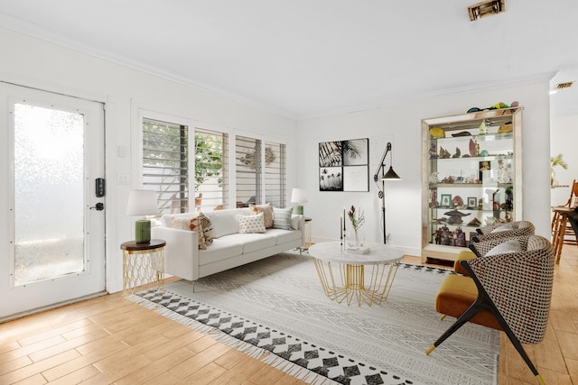 living area with ornamental molding, light wood-type flooring, and visible vents