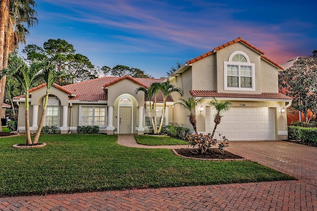 mediterranean / spanish home with a tiled roof, stucco siding, decorative driveway, a yard, and an attached garage