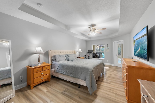 bedroom with ceiling fan, a raised ceiling, light hardwood / wood-style floors, and a textured ceiling