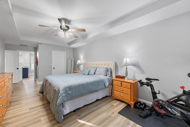 bedroom with a raised ceiling, a textured ceiling, ceiling fan, and light hardwood / wood-style floors