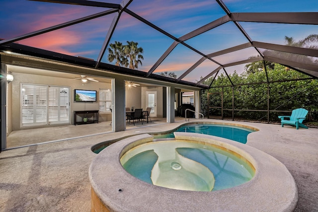 pool at dusk featuring ceiling fan, glass enclosure, an in ground hot tub, and a patio