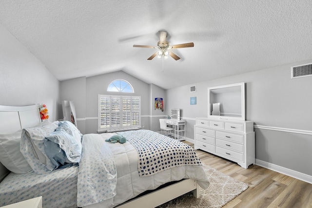 bedroom with a textured ceiling, vaulted ceiling, ceiling fan, and light wood-type flooring