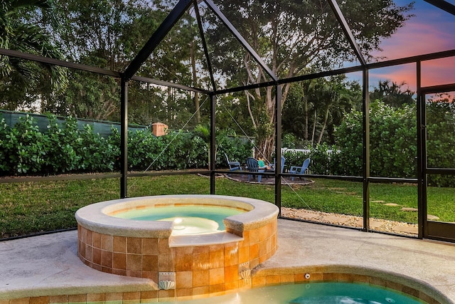 pool at dusk with an in ground hot tub, glass enclosure, and a patio