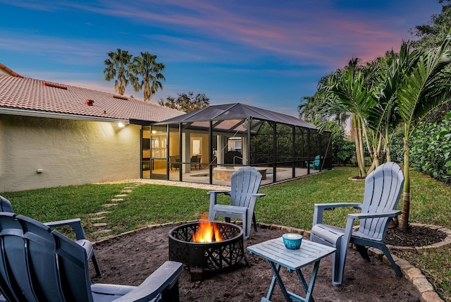 yard at dusk with a patio area, glass enclosure, and an outdoor fire pit